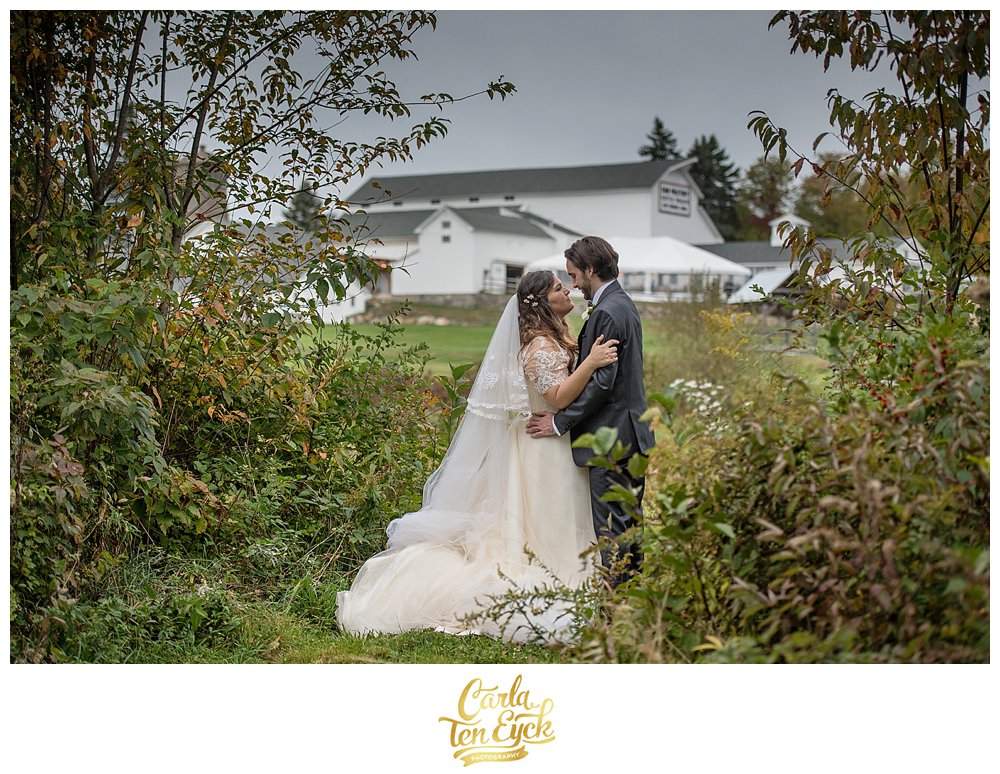 A couple embraces in a field with the white barn in the background at their wedding at South Farms in Morris CT