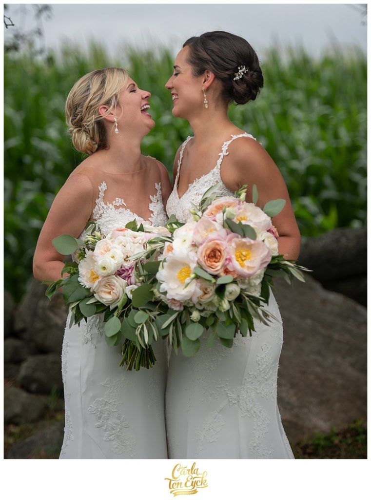 Two brides laugh holding wedding bouquet with peonies and ranunculus and dahlias by Hana Floral at Jonathan Edwards Winery 