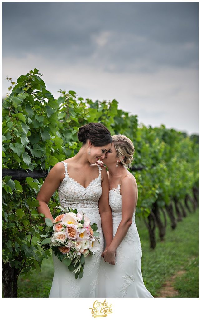 Two brides cuddle in the vines at Jonathan Edwards Winery Wedding with soft pink wedding bouquet by Hana Floral