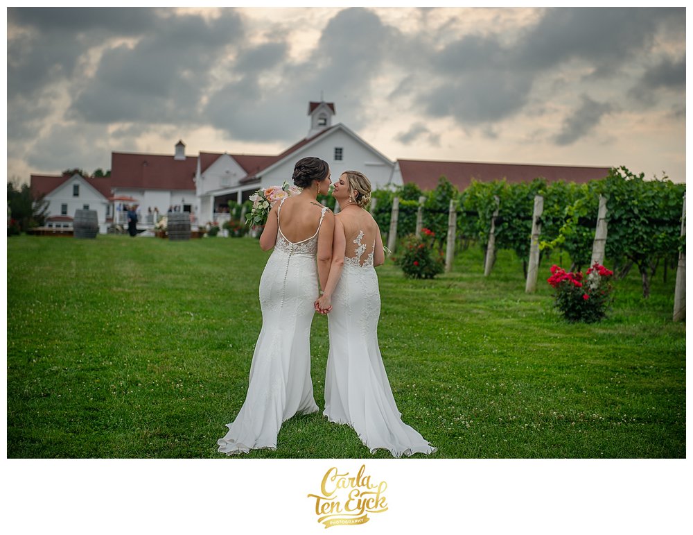Two brides kiss with Jonathan Edwards Winery in the background on their wedding day