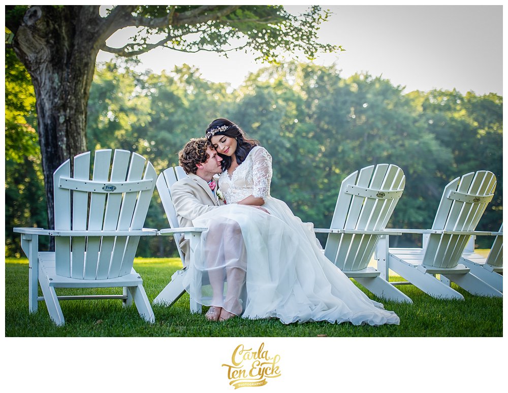 Bride and groom cuddle on Adirondack chairs at Smith Farm Garden on their wedding day in East Haddam CT