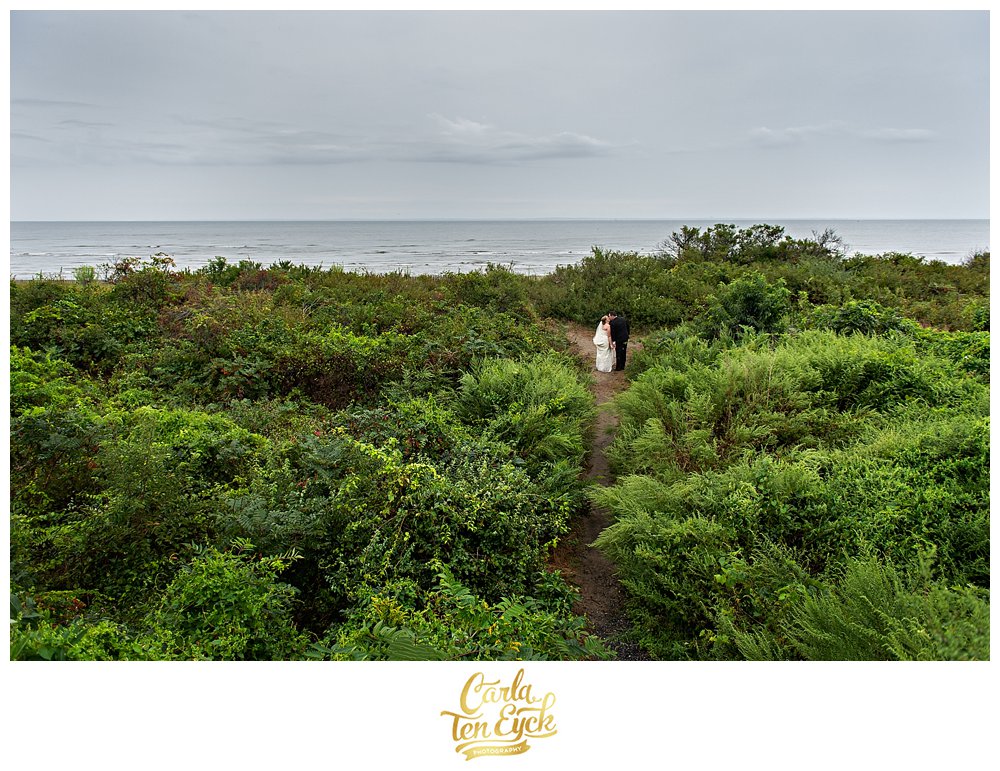 Bride and groom kiss on a path to the beach during their tented CT wedding in Lordship