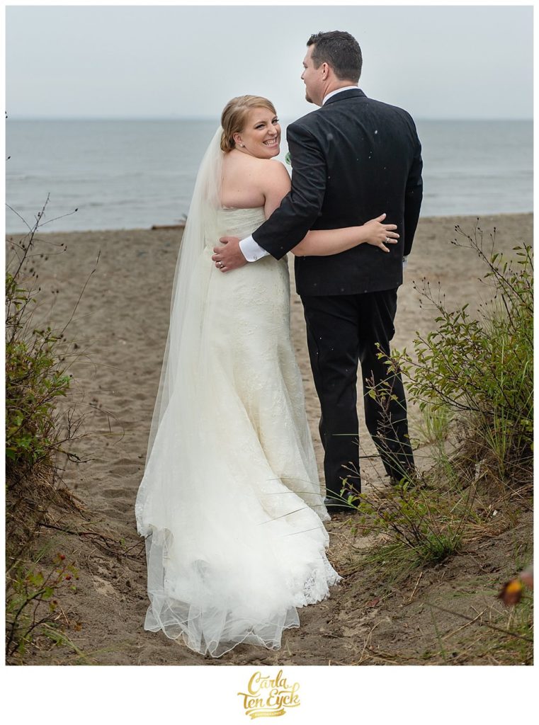 Happy bride and groom on the beach in the rain at their tented CT wedding in Lordship