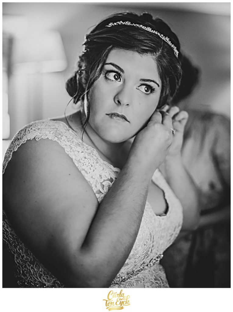 Bride puts on earrings in her lace wedding gown
