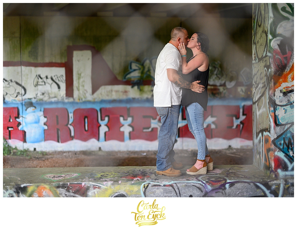 Couple kisses during their CT engagement session with graffiti walls in Portland CT