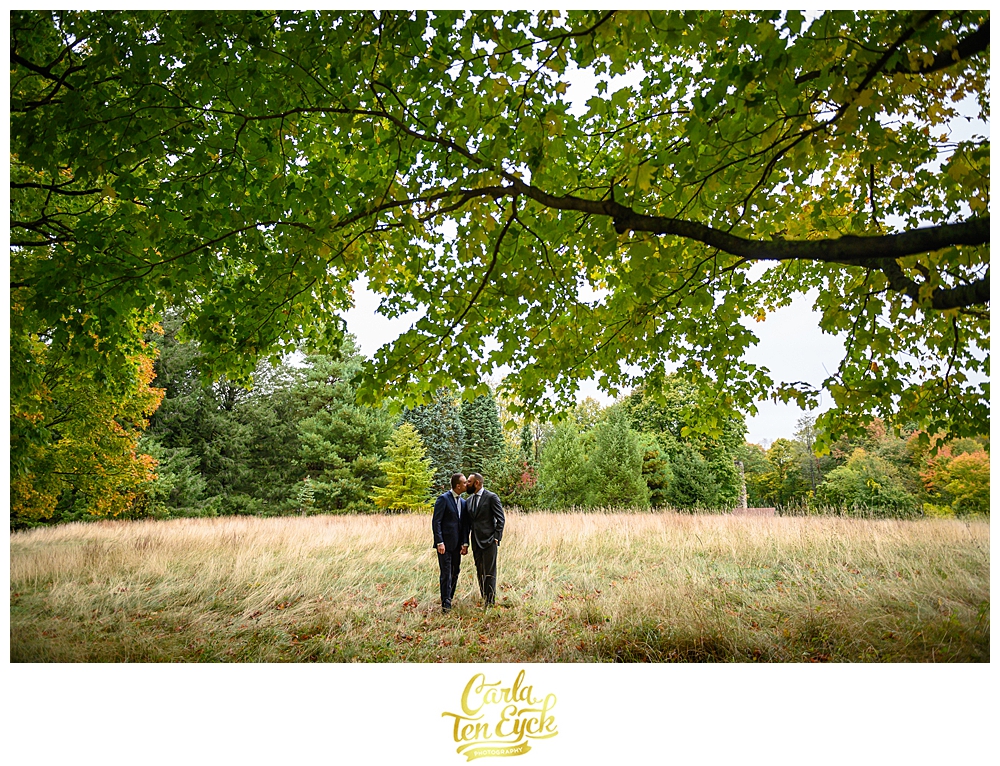 Two grooms kiss under a tree at their wedding at the Eustis Estate in Milton MA