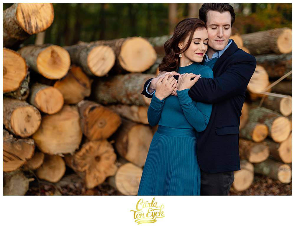A couple snuggles during their engagement session at Smith Farm Gardens in East Haddam CT by the wood pile
