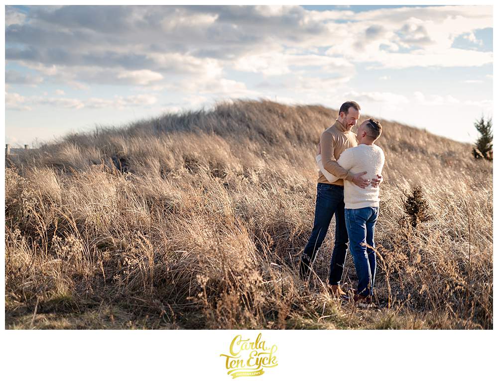 Two grooms in the dunes during their winter beach engagement session at Silver Sands beach in Milford CT