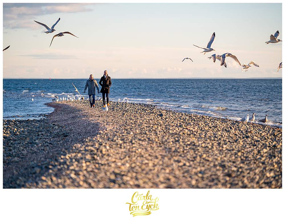 Two grooms walk the beach during their winter engagement session at Silver Sands beach in Milford CT