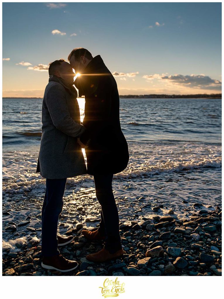 Two grooms cuddle during their winter engagement session at Silver Sands beach in Milford CT