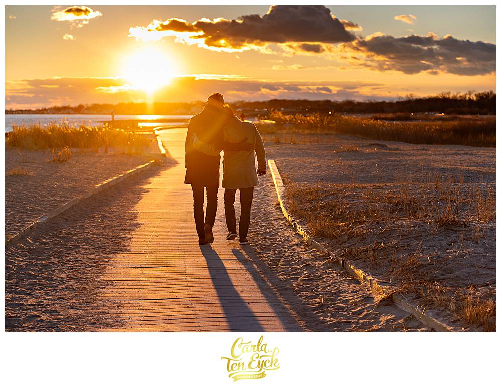 Two grooms cuddle at sunset during their winter engagement session at Silver Sands Beach in Milford CT