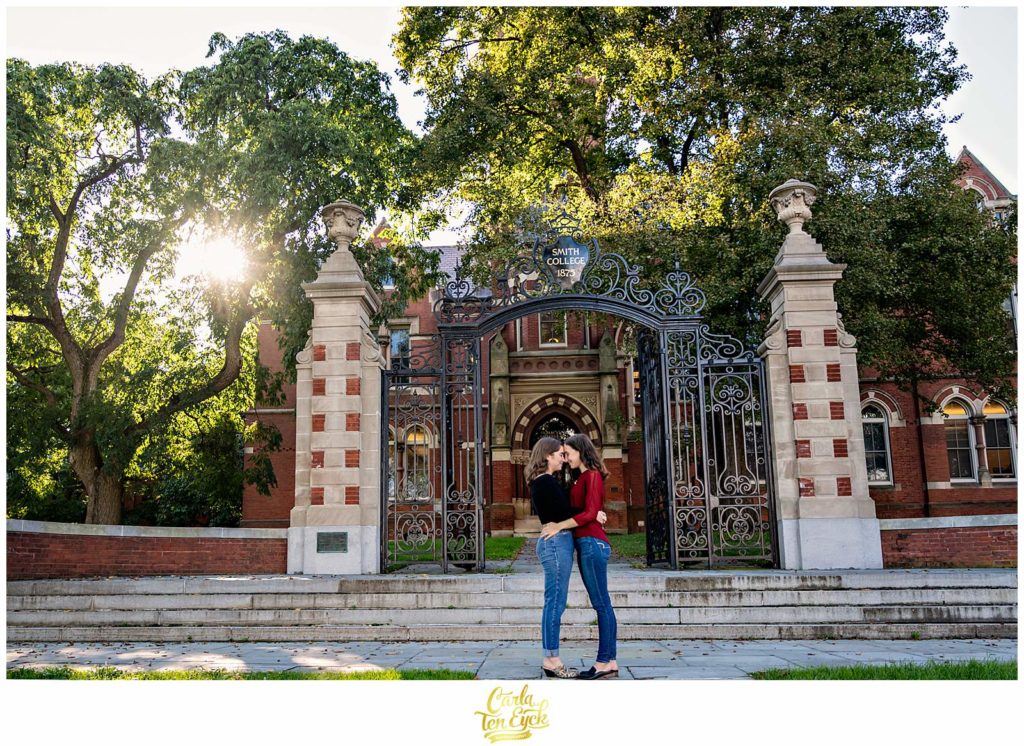 Two brides to be snuggle at the gates of Smith College in Northampton MA during their engagement session.