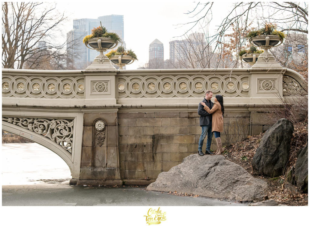 A couple poses for their winter engagement session by the iconic Bow Bridge in Central Park in NYC