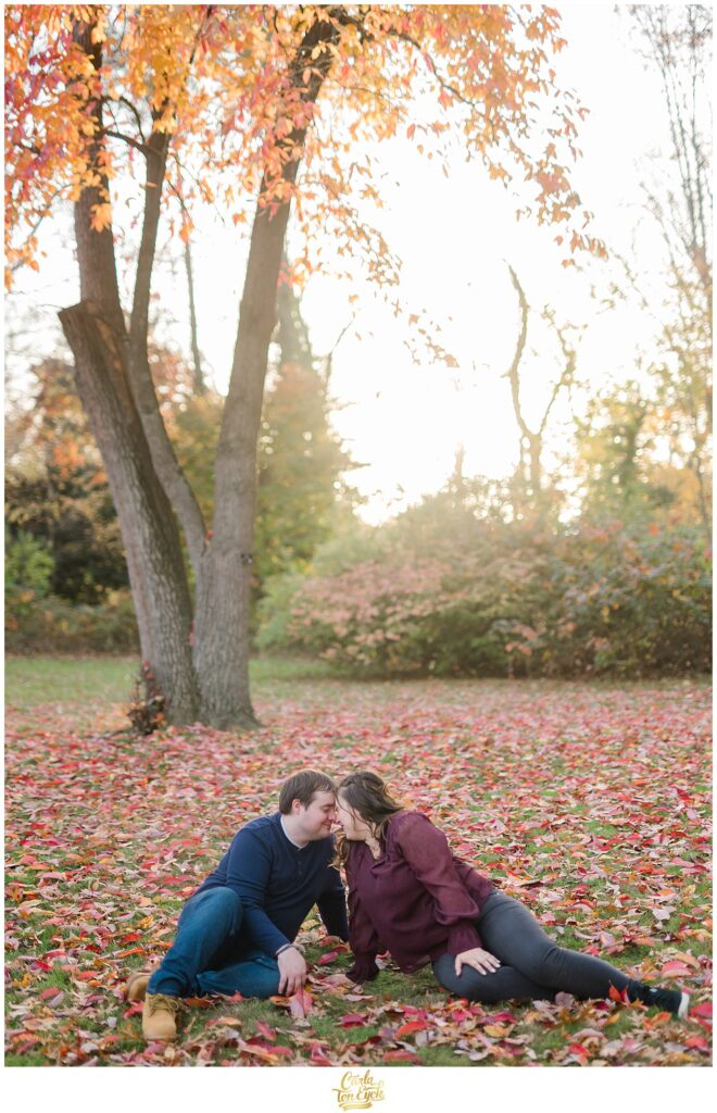 A couple lays in the leaves during their fall engagement session at Elizabeth Park in Hartford CT