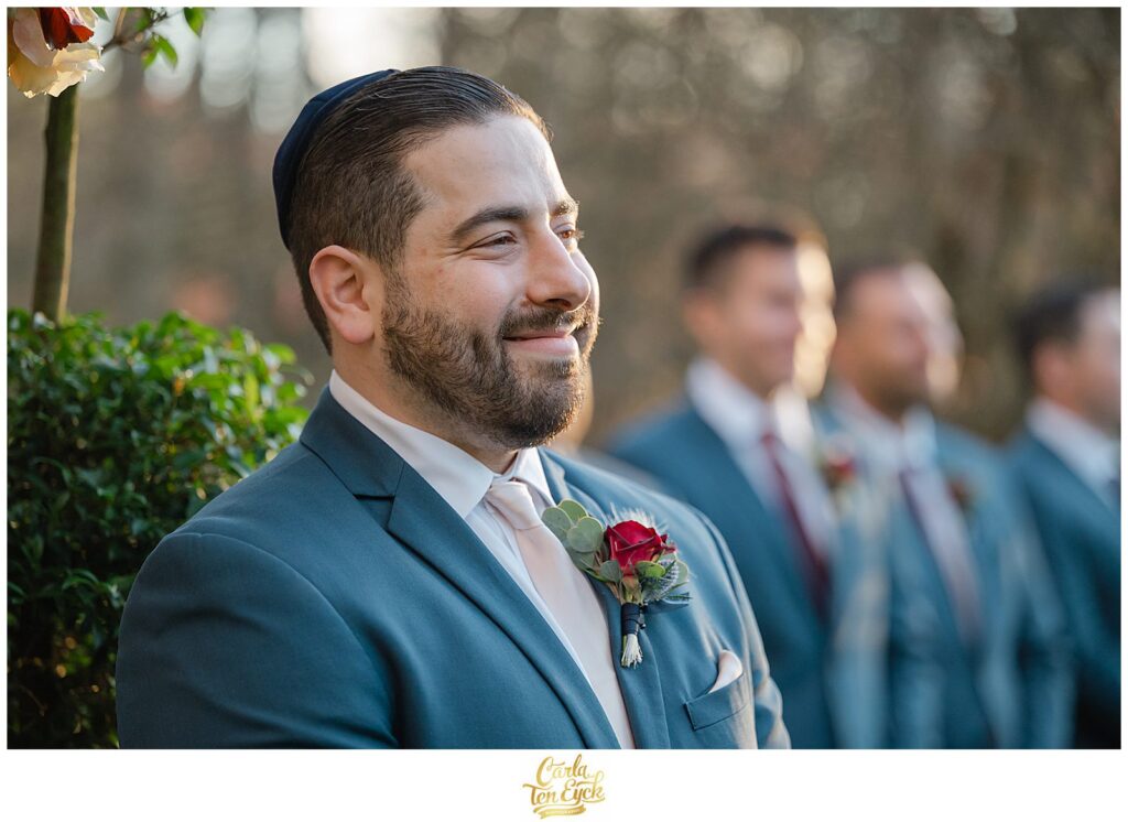 A groom smiles as he watches his bride walk down the aisle at his  autumn lord Thompson Manor wedding in Thompson CT