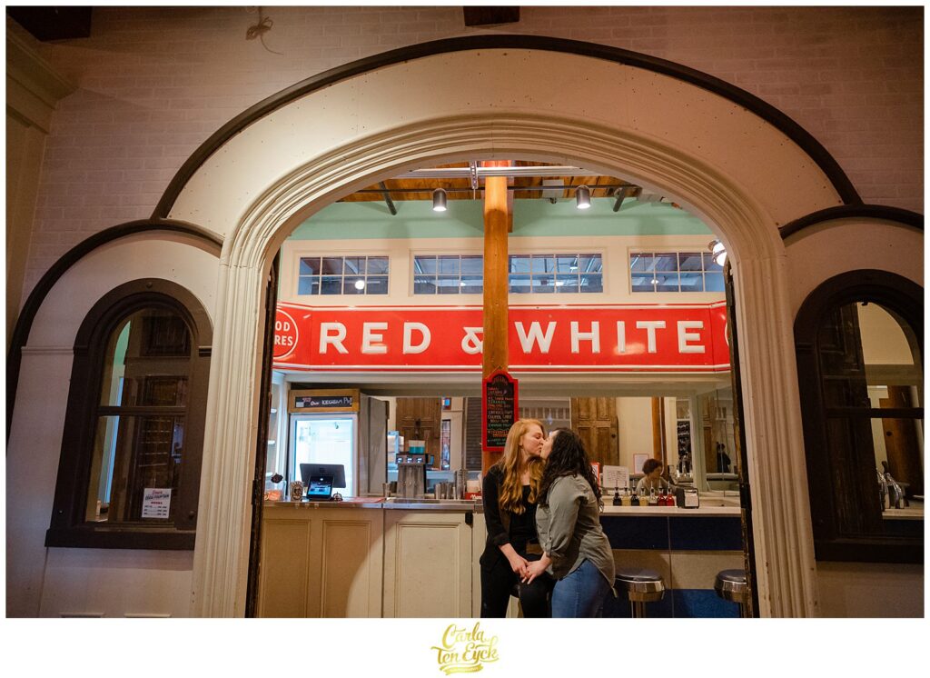 Two brides sit at the counter of Red and White  during their engagement session at  Mill NO. 5 in Lowell MA