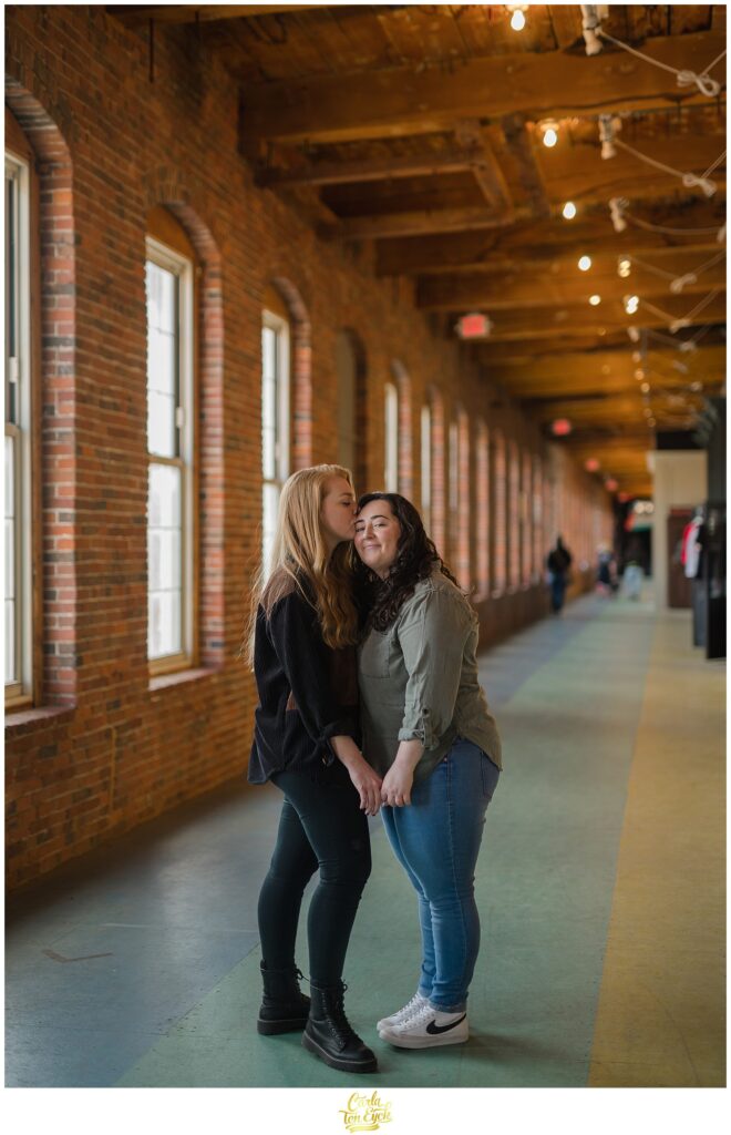 Two brides cuddle during their engagement session at  Mill NO. 5 in Lowell MA