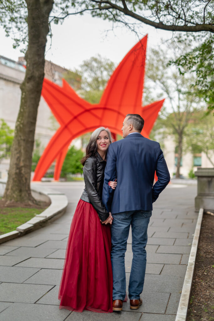 A couple poses for a photo during their Hartford City Hall elopement with a true to color editing style that showcases the Calder Stagosaurus sculpture