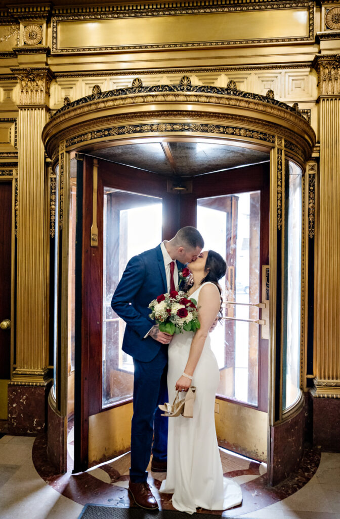 A couple kisses in the gold revolving doors after their elopement at Hartford City Hall in Hartford CT