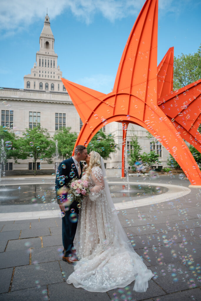 A bride and groom kiss amidst bubbles at their Hartford City Hall elopement in front of the Stegosaurus statue in Hartford CT