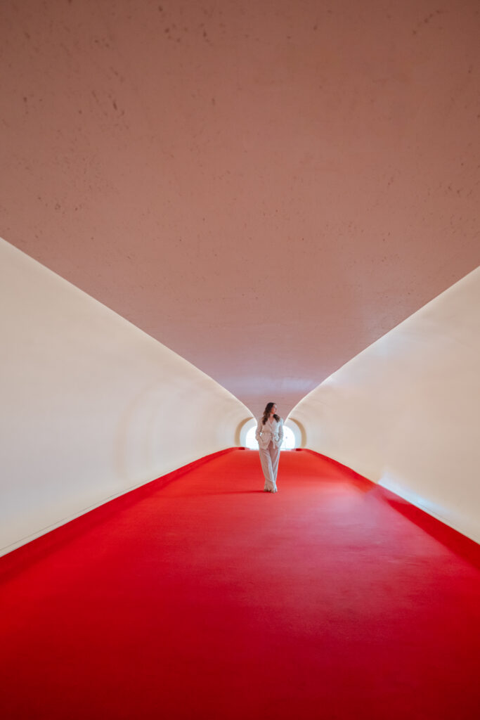Wide shot of Carla Giorgio walking through the retro red carpet hallway of the TWA Hotel for her NYC branding shoot