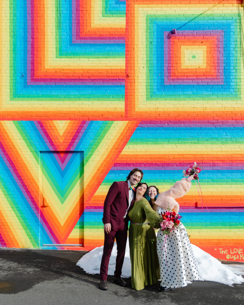 A queer bride poses for photos with her kids in front of a rainbow mural in Hartford CT