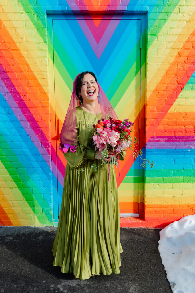 A bride in her chartreuse wedding dress with her hot pink veil and colorful wedding bouquet in front of a rainbow mural in Hartford CT