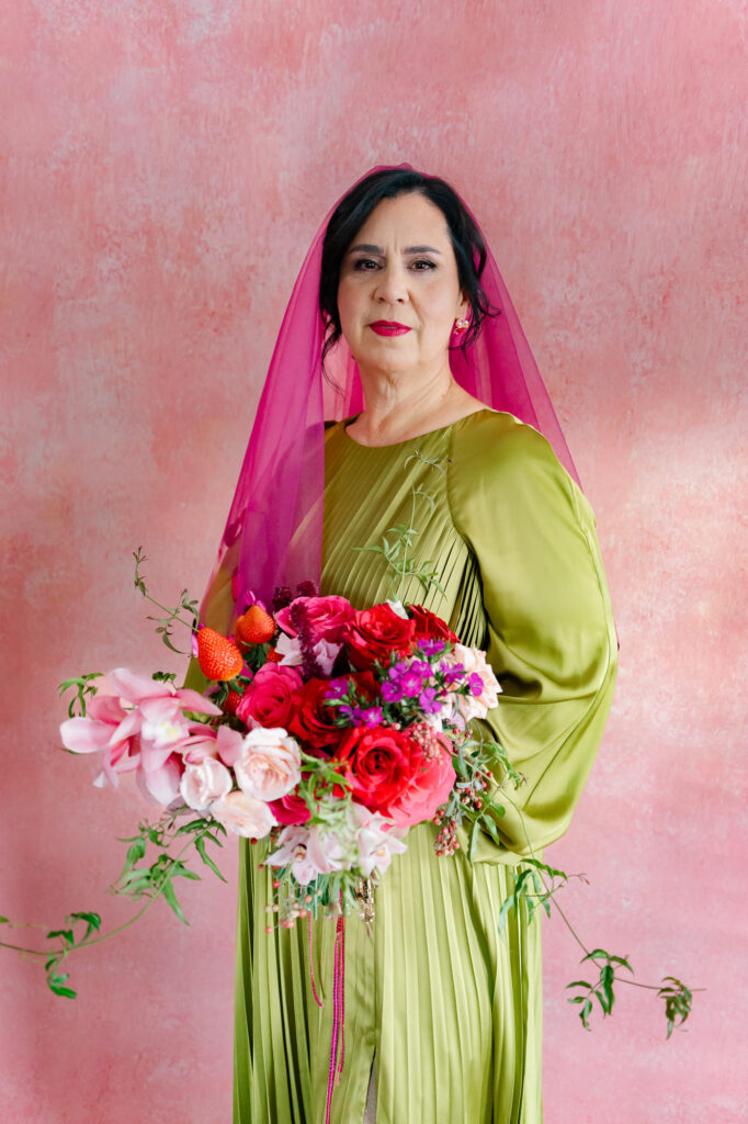 A queer brides poses in her colorful chartreuse wedding gown with a pink and red wedding bouquet with strawberries and a hot pink veil for her Hartford City Hall elopement